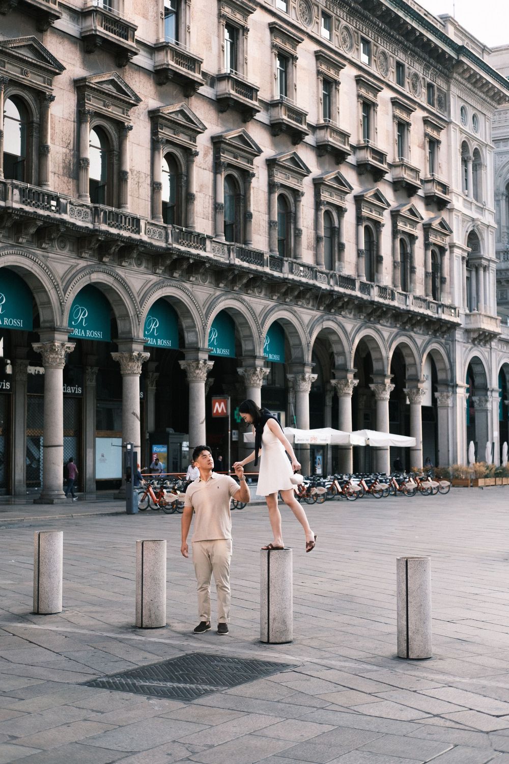 Couple dancing in a grand European piazza with arched colonnades and historic architecture in Milan, Italy.
