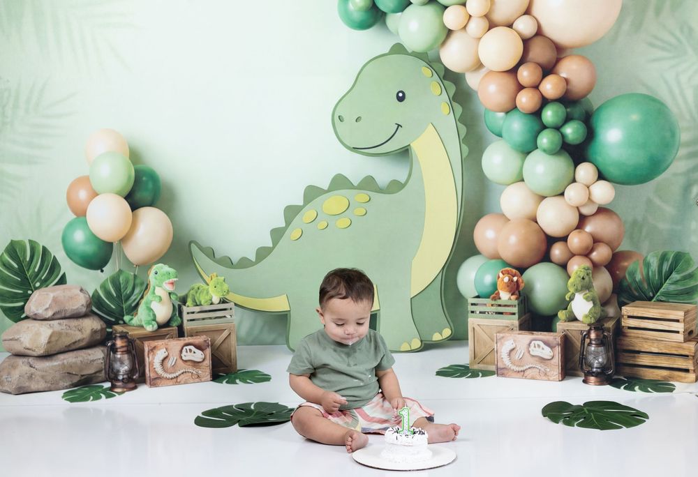 Baby's first birthday cake smash with dinosaur theme, green balloons, tropical leaves, and adorable dino backdrop.