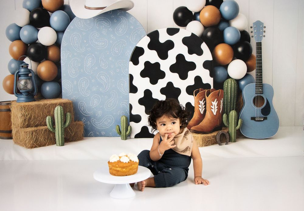 Baby's first birthday cake smash with western cowboy theme, balloons, guitar, and hay bales backdrop.
