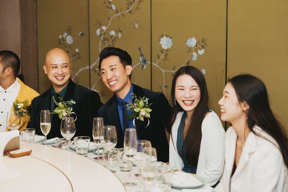 Guests laughing and smiling together at an elegant wedding reception dinner table with champagne glasses.