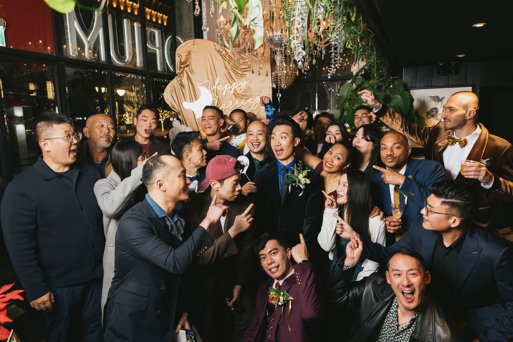 A joyful group of people celebrating at a wedding reception outside a MUFO venue, posing and cheering together.