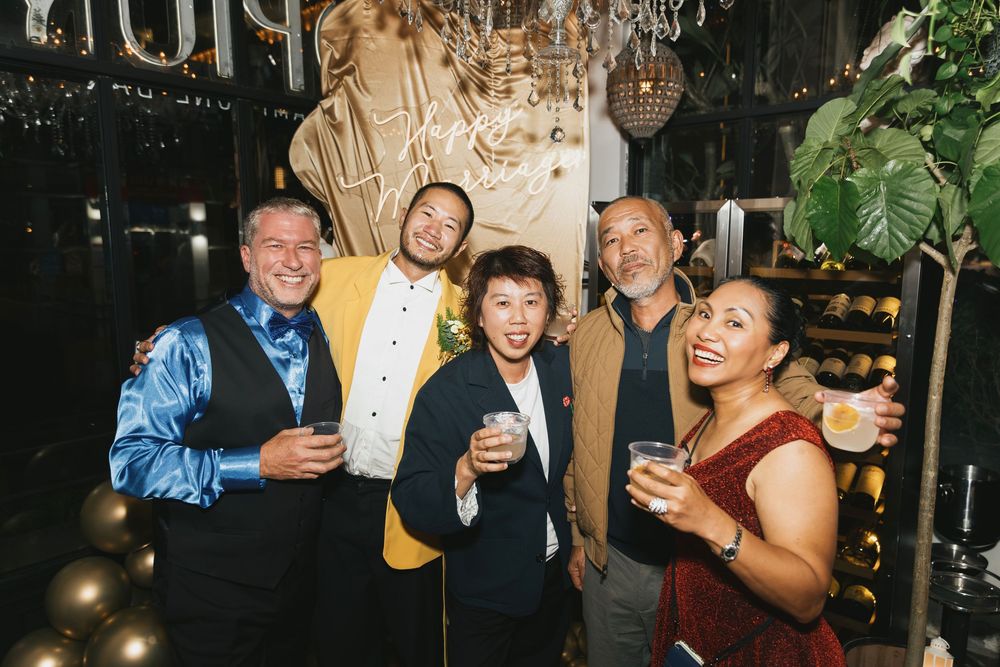 Five people smiling and holding drinks at a festive celebration party with elegant decor and warm lighting.