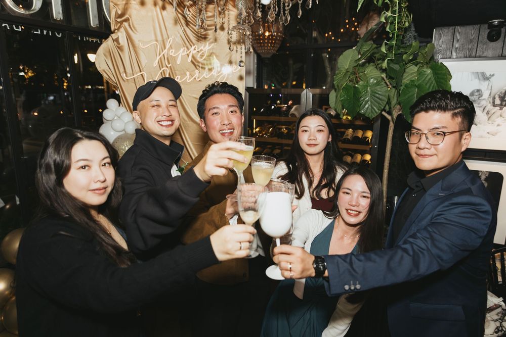 Group of six friends toasting with cocktails at a festive party celebration in a decorated venue.