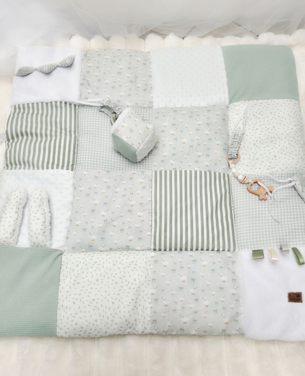 Sage green and white patchwork baby play mat with stripes, dots, and gingham patterns, featuring small toys.