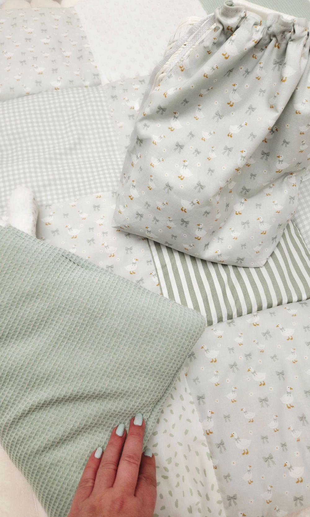 Soft sage green baby nursery fabrics including gingham, stripes, and floral prints with a drawstring bag and waffle blanket.