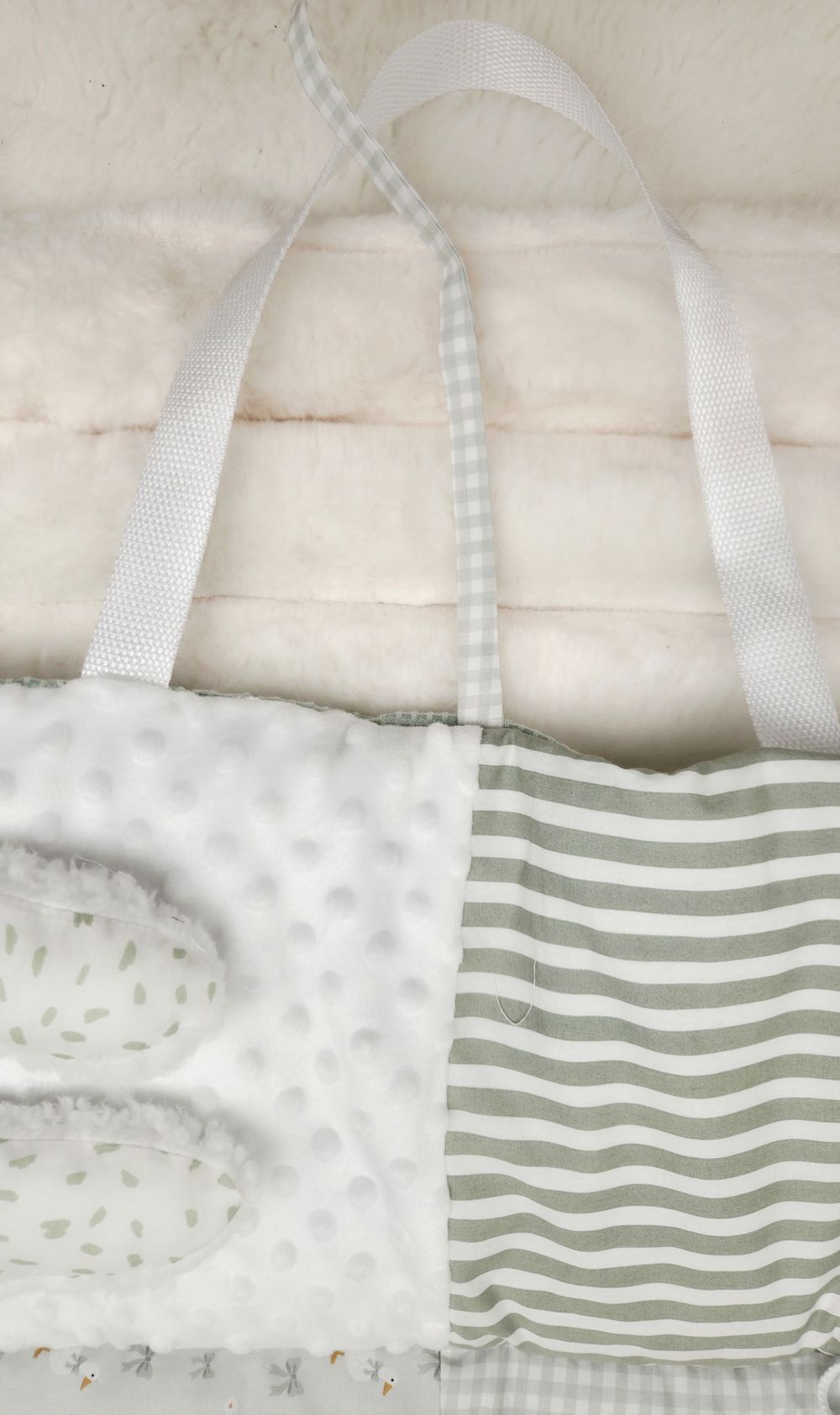Handmade baby tote bag with white minky dot and sage green striped fabric panels, white webbing handles, on fluffy background.