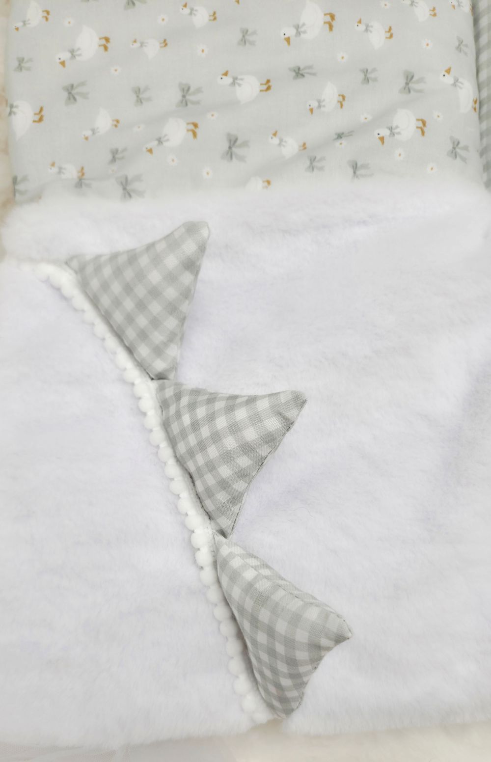 White fluffy baby blanket with gray gingham triangle decorations and a soft patterned fabric top featuring small animals.