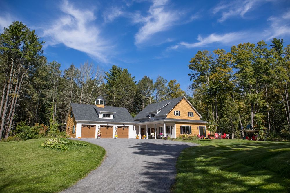 Beautiful craftsman-style home with three-car garage and cedar siding set among fall foliage trees in New England.