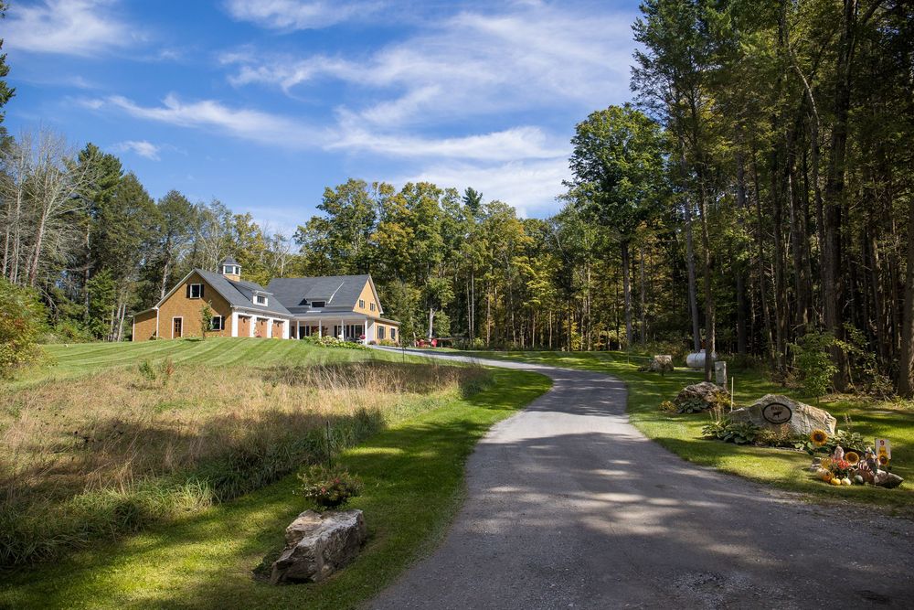 Charming country home with a winding gravel driveway surrounded by colorful autumn trees and open green lawn.