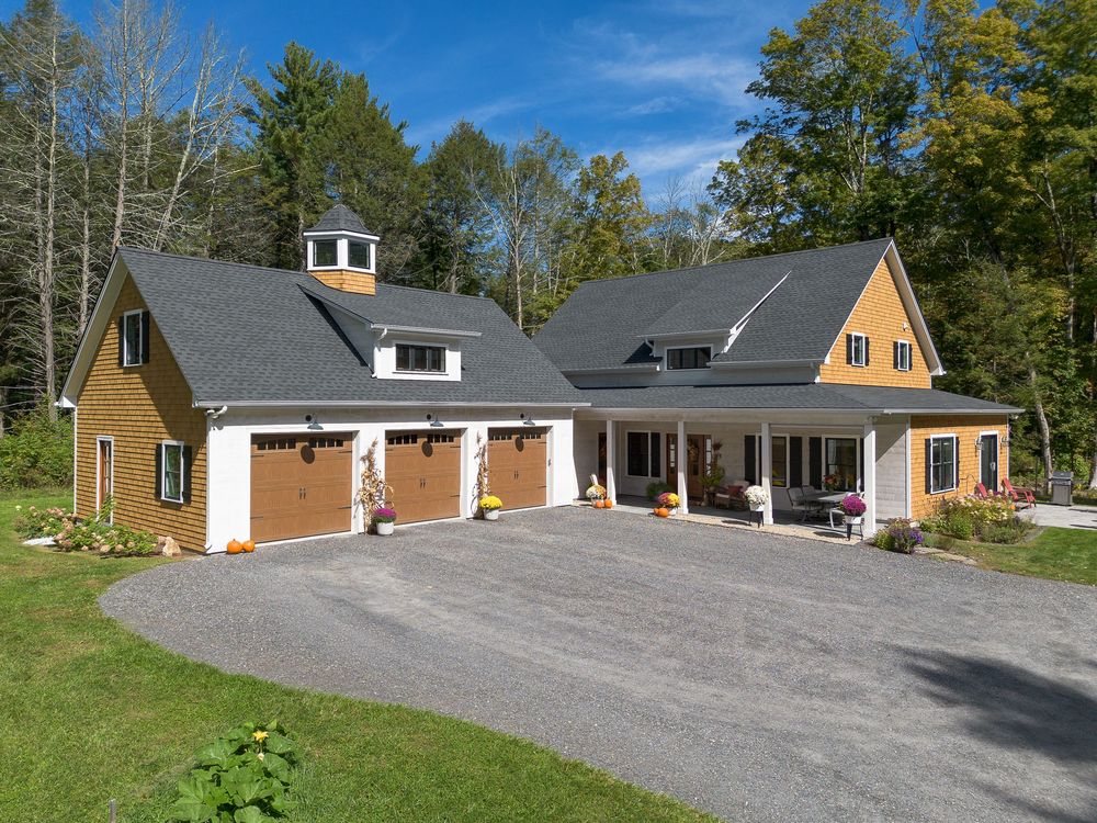 Beautiful cedar craftsman home with three-car garage, cupola, and covered porch surrounded by colorful fall trees.