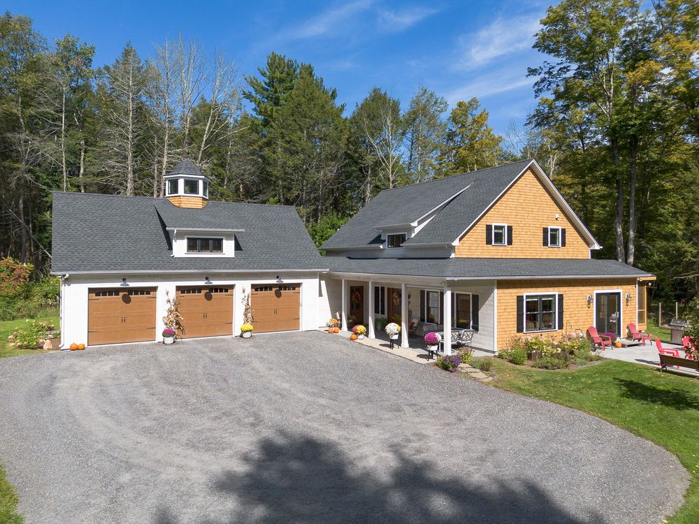 Attractive cedar craftsman home with three-car garage, covered porch, and colorful autumn foliage in New England.