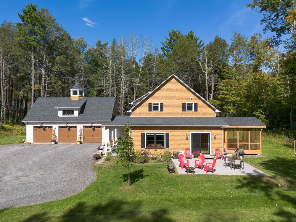 Gorgeous craftsman-style home with covered porch, red Adirondack chairs, and lush lawn surrounded by forest trees.