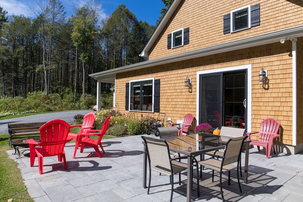 Inviting patio with red Adirondack chairs and outdoor dining furniture beside a warm cedar-sided home with black shutters.