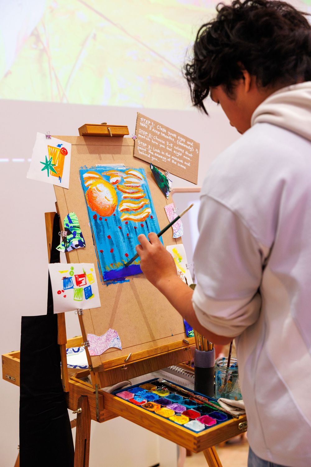Young artist painting colorful canvas on wooden easel with watercolors and brushes in art studio.
