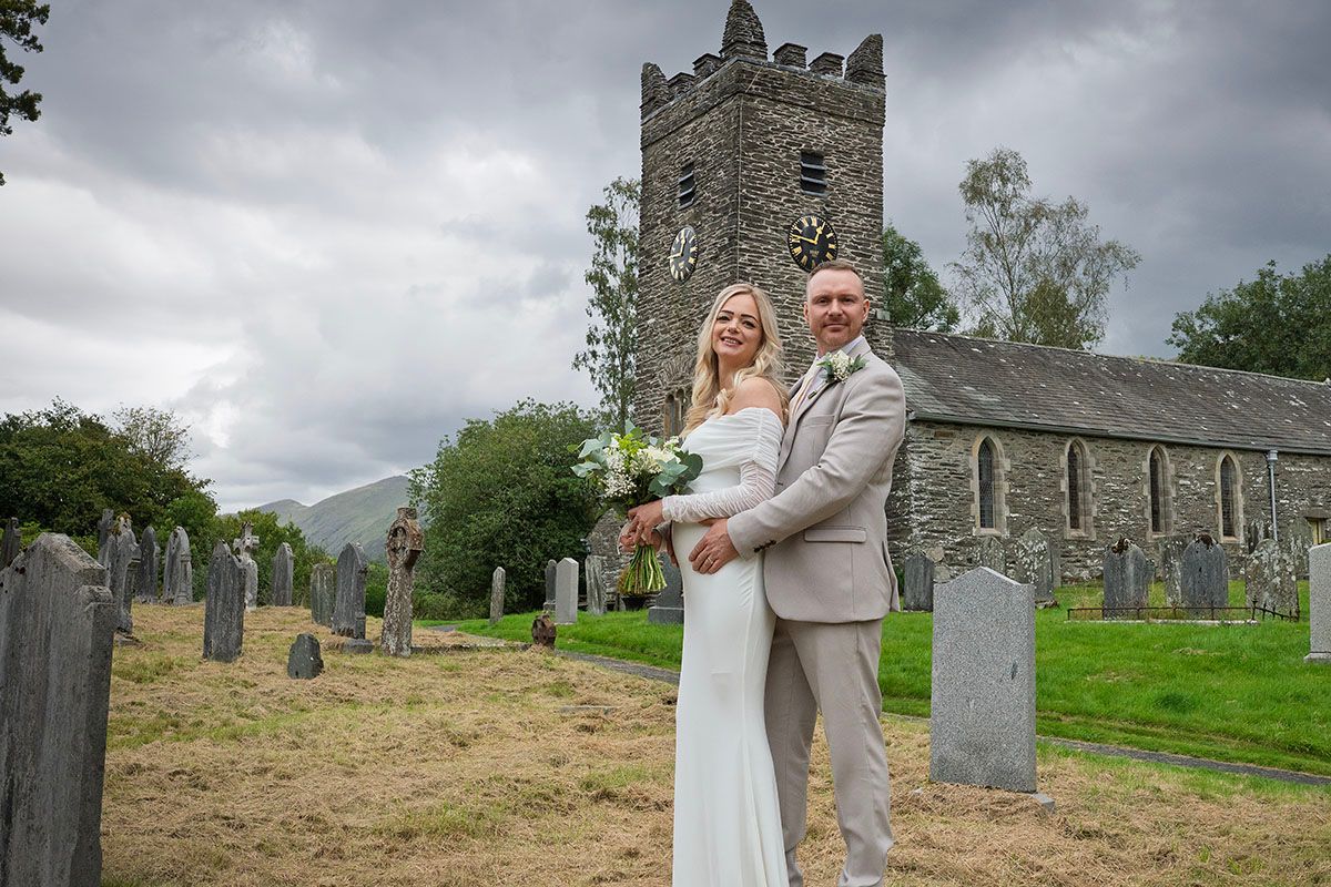 Bride and groom pose in a historic church graveyard on their elopement wedding day in the Lake District