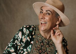 Smiling person wearing a straw hat and floral green top, posing cheerfully in a studio portrait.