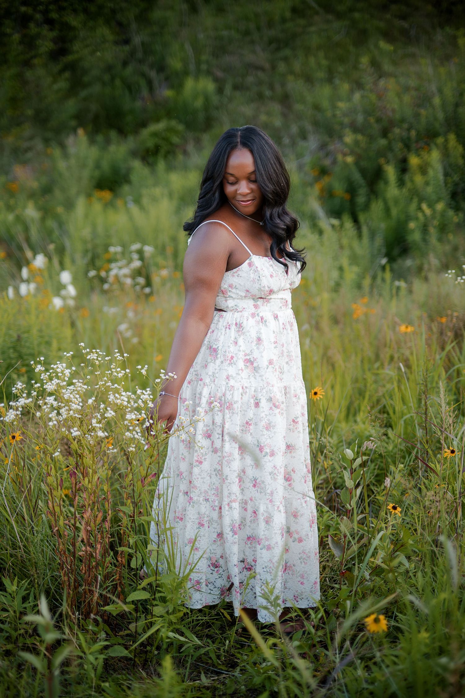 A young Black woman in a floral maxi dress stands gracefully among wildflowers in a lush green meadow.