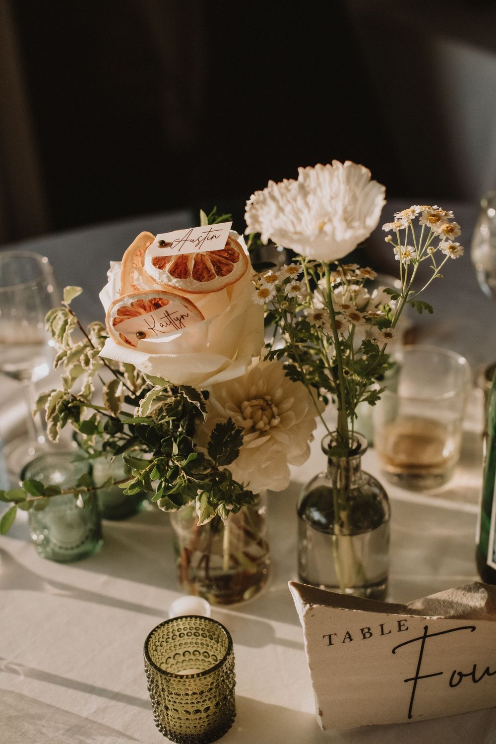 Elegant wedding table centerpiece with white roses, wildflowers, and dried citrus in glass bud vases with a Table Four sign.