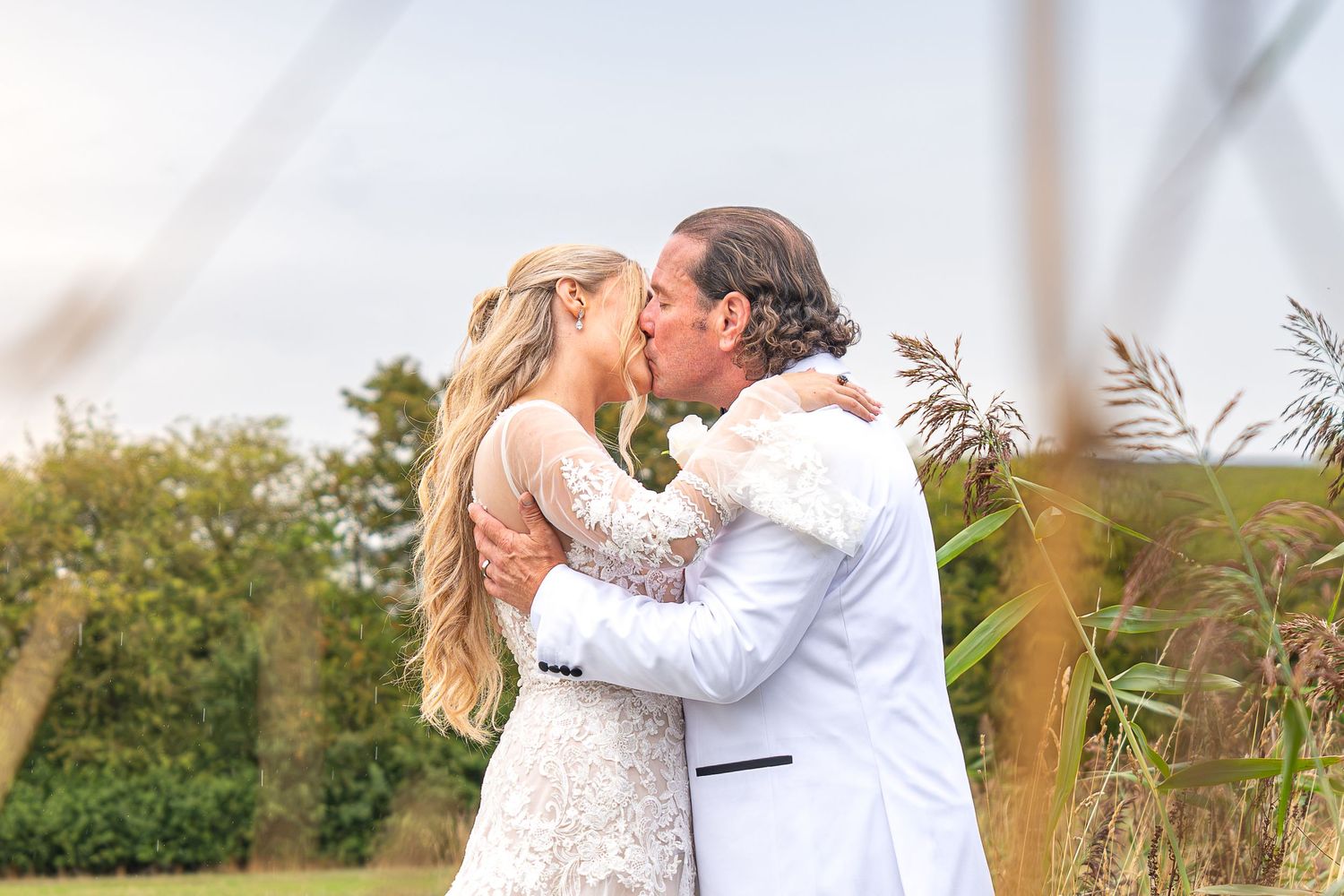 Bride and groom share first kiss outdoors at wedding ceremony with tall grass and greenery in background.Yorkshire, Sheffield, Lincolnshire,