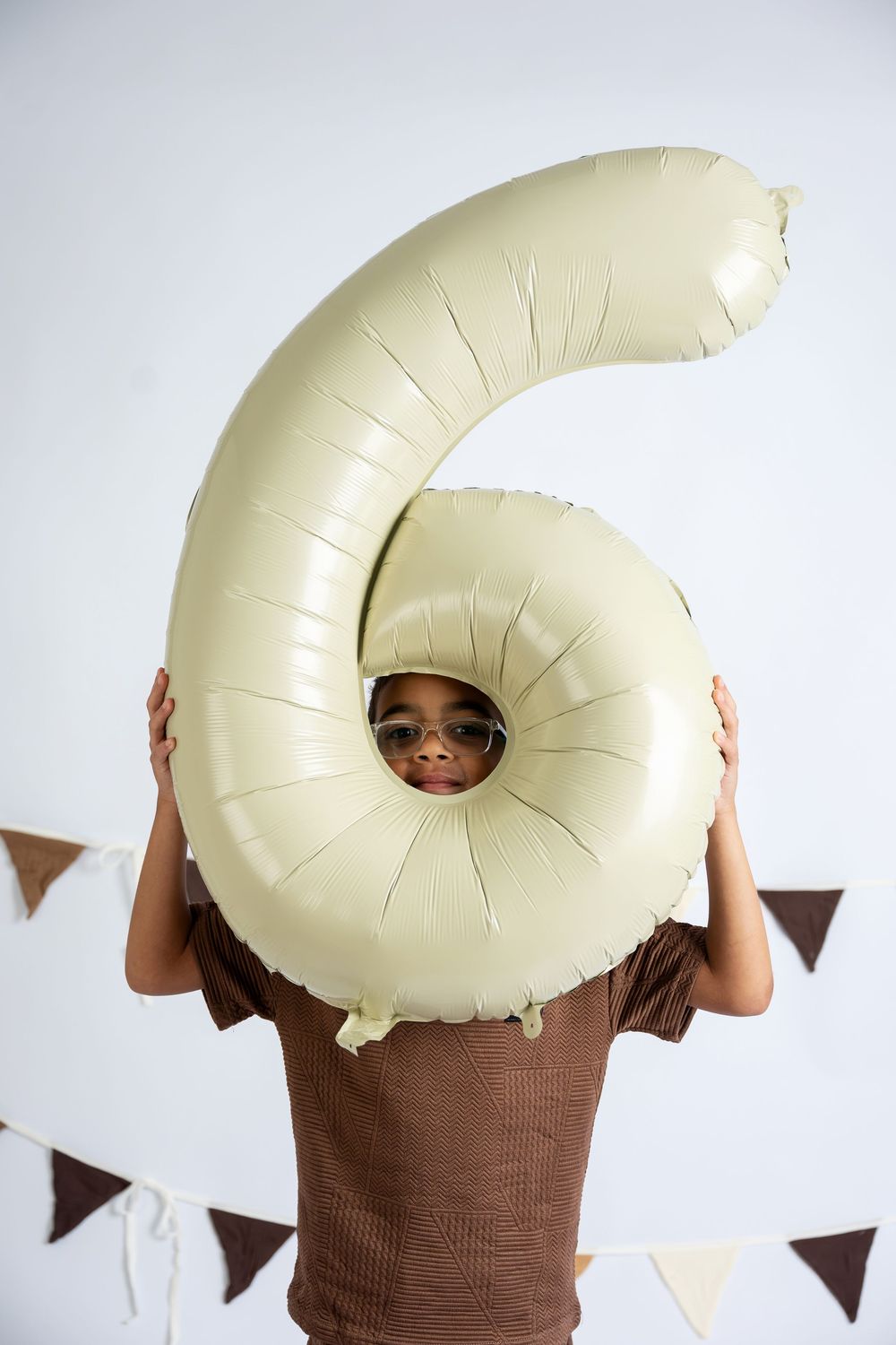 A child peers through the hole of a large number 6 balloon at a birthday party celebration.
