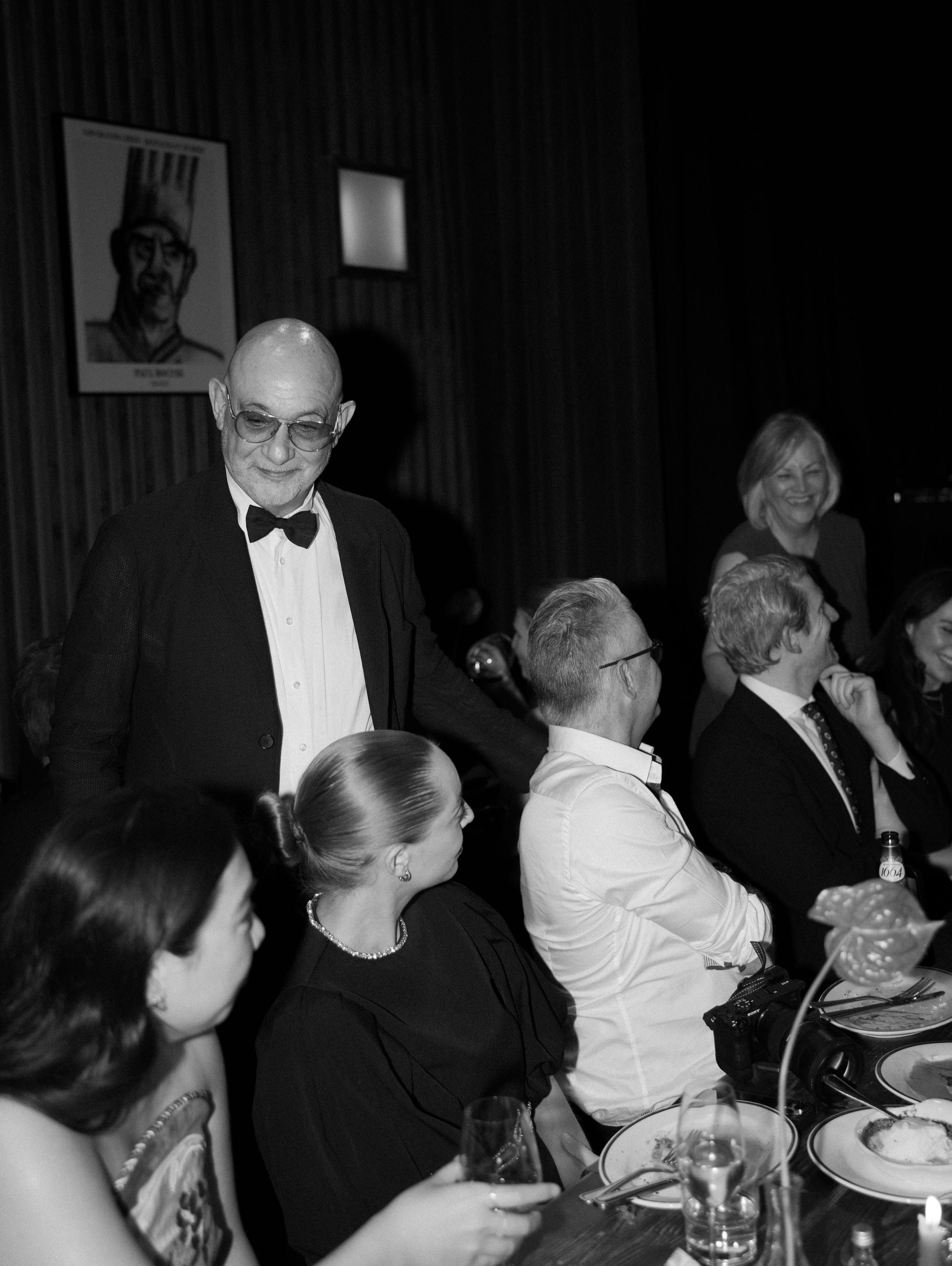 Black and white photo of elegantly dressed guests at a formal dinner gala event.