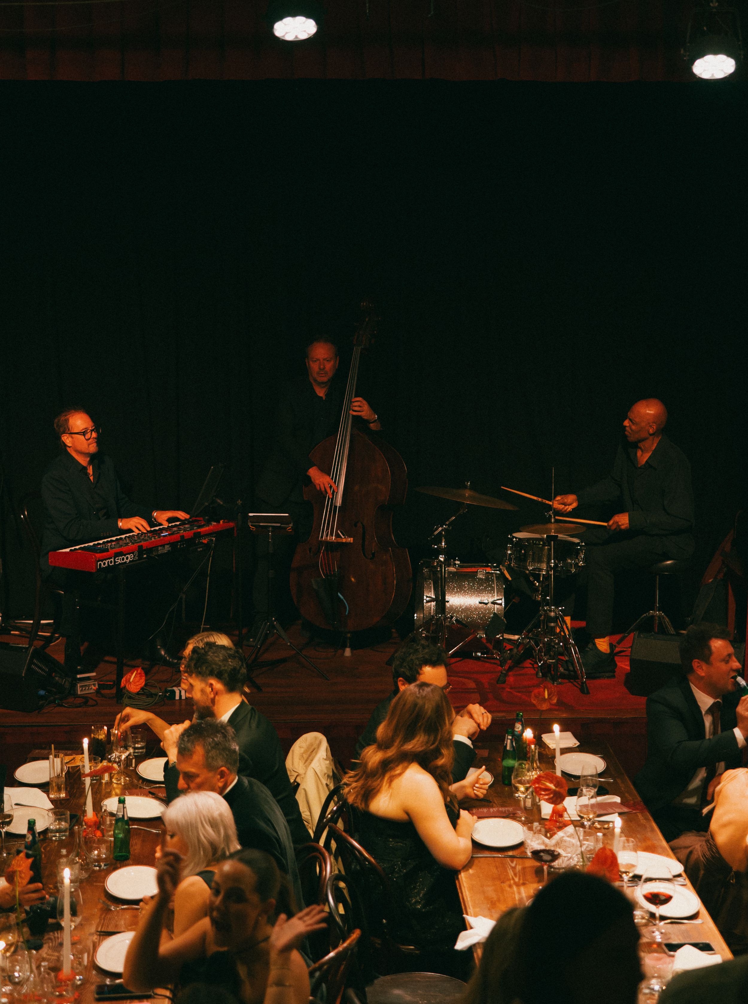 Jazz quartet performs on stage at elegant candlelit dinner event with guests seated at long tables.