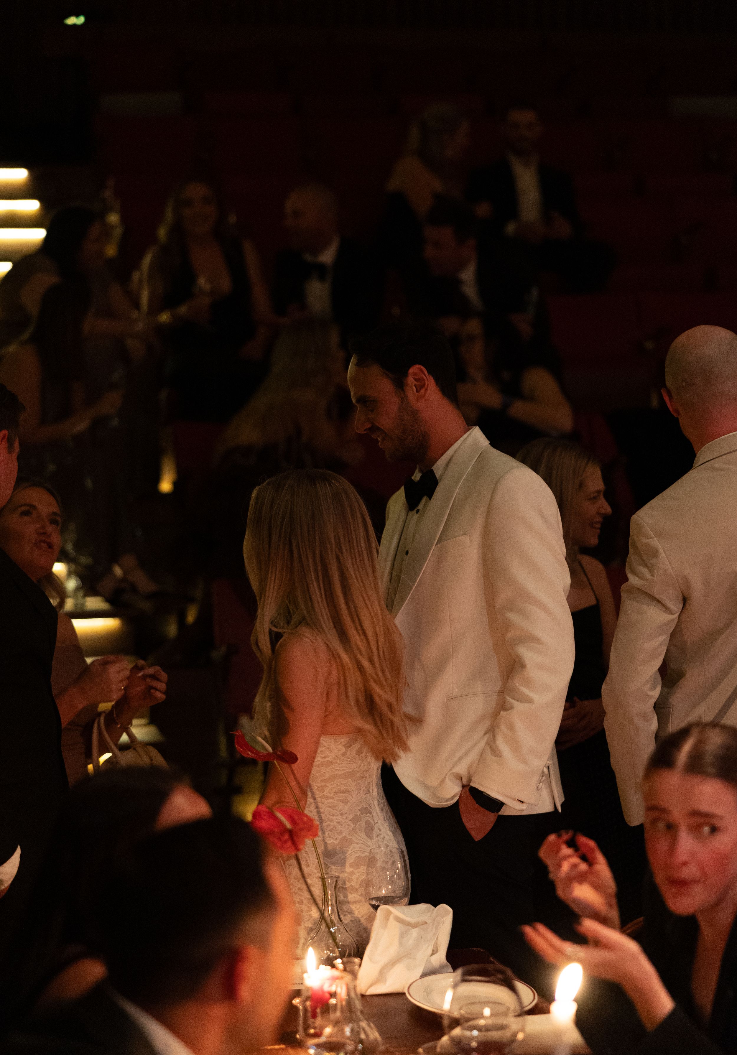 Elegant couple sharing an intimate moment at a formal gala dinner event with candlelit tables and guests.