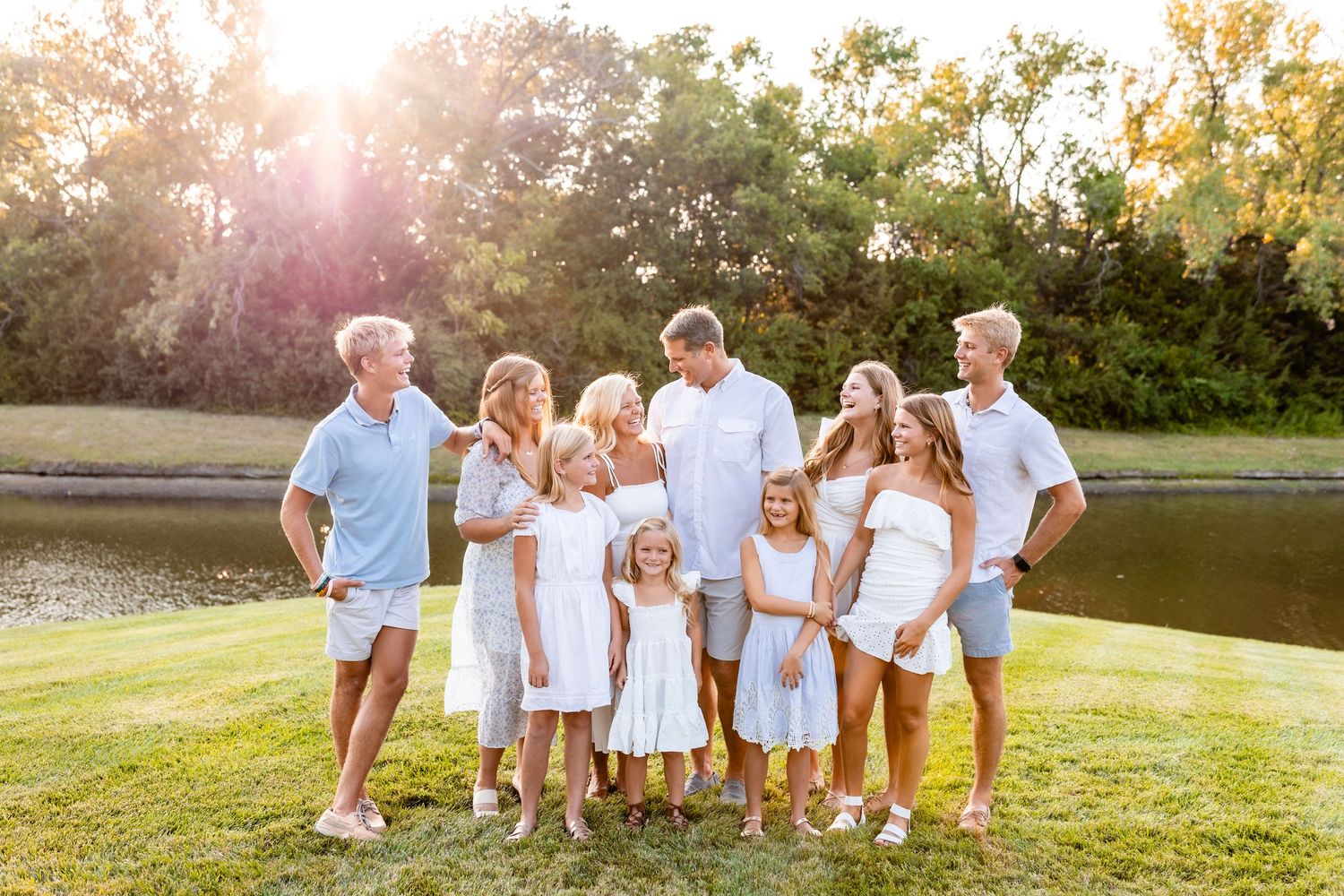 A multi-generational family poses together in white outfits at sunset by a lake.