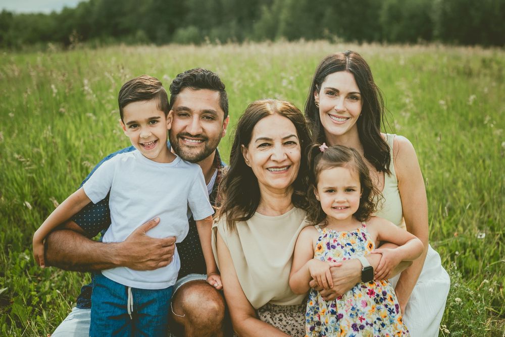 Extended family of five posing together in a lush green field, smiling warmly at the camera. St Albert Family Photographer