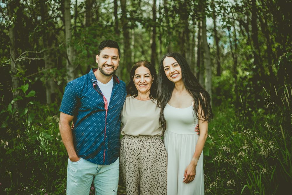 A man and two women smiling together in a lush green forest setting for a family portrait photo. St Albert Family Photographer