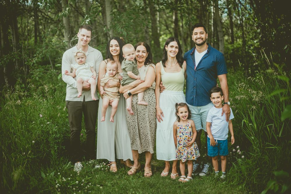 Large extended family group portrait taken outdoors in a forested area with young children and babies. St Albert Family Photographer