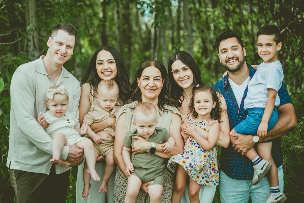 Extended family portrait with parents grandparent, and young children posing in a green wooded outdoor setting St Albert Family Photographer