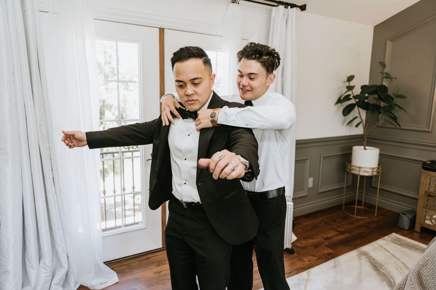 Groomsman helping Paul put on his tuxedo jacket