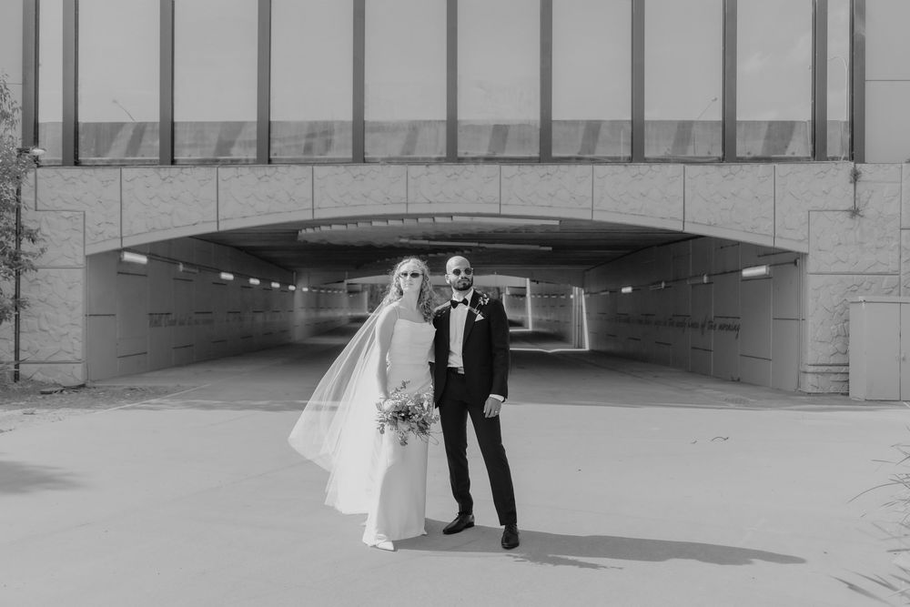 Black and white photo of a bride and groom standing together outside a modern building on their wedding day.