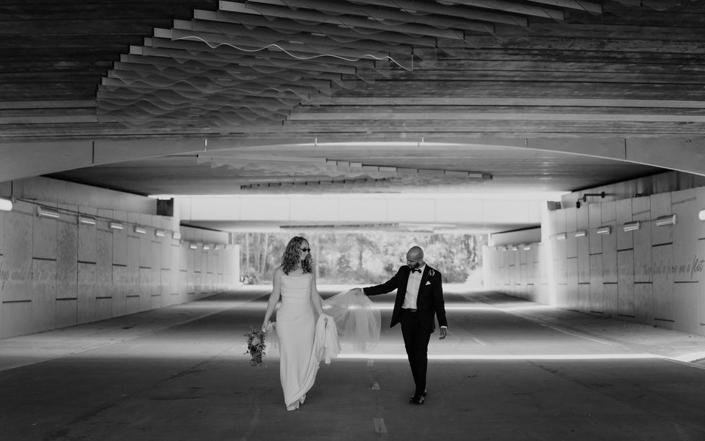 Black and white photo of bride and groom walking hand in hand through an urban tunnel on their wedding day.