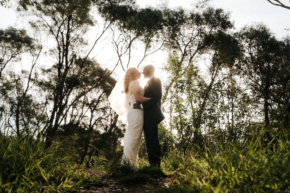 Bride and groom silhouetted against golden sunlight in a lush forest setting during their outdoor wedding ceremony.