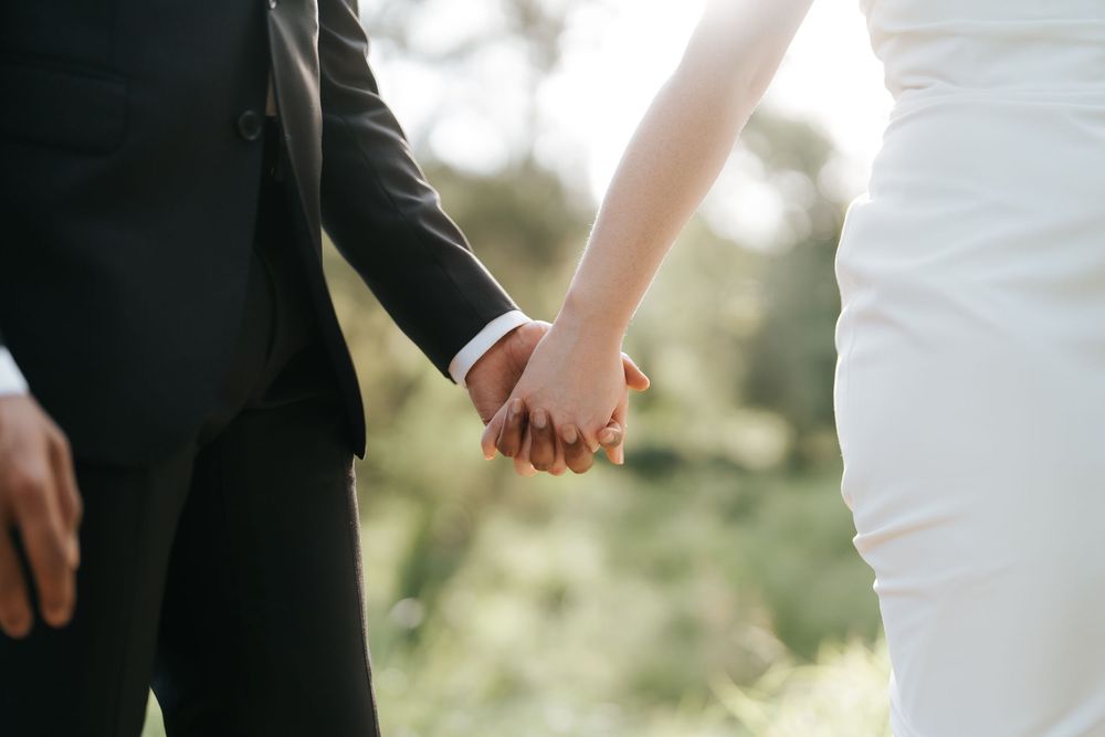 Bride and groom holding hands outdoors on their wedding day, wearing white dress and black tuxedo.