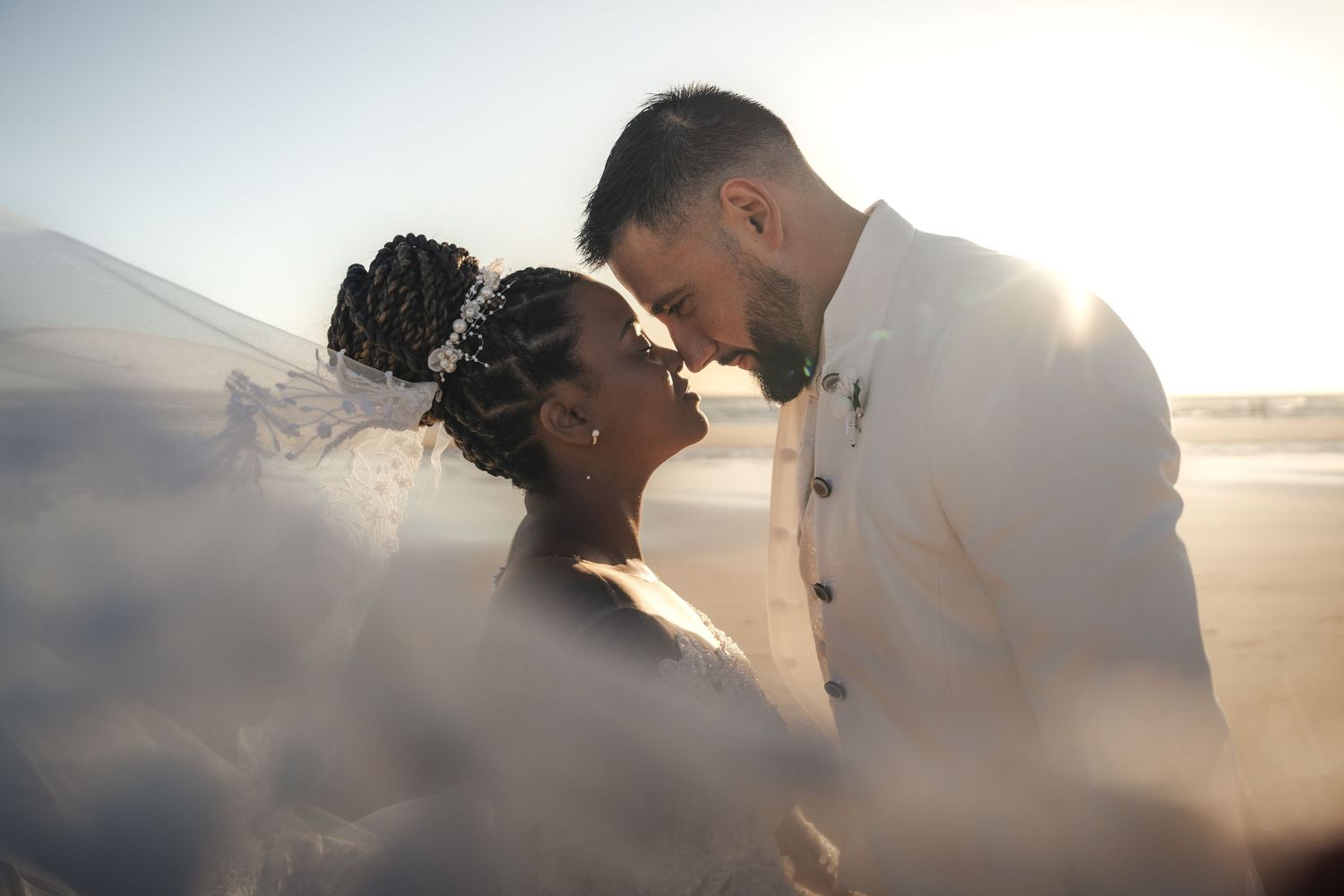 A bride and groom share an intimate moment, touching foreheads in soft golden backlight on their wedding day.