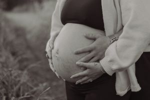 Black and white close-up of pregnant womans bare baby bump being cradled by both hands outdoors.
