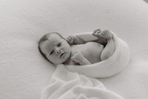 Black and white newborn portrait of baby wrapped in soft white fabric lying on fluffy blanket.