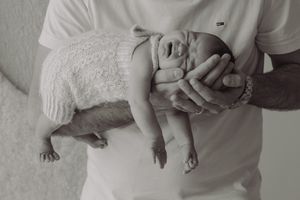 Black and white photo of father cradling sleeping newborn baby in his arms against white shirt.