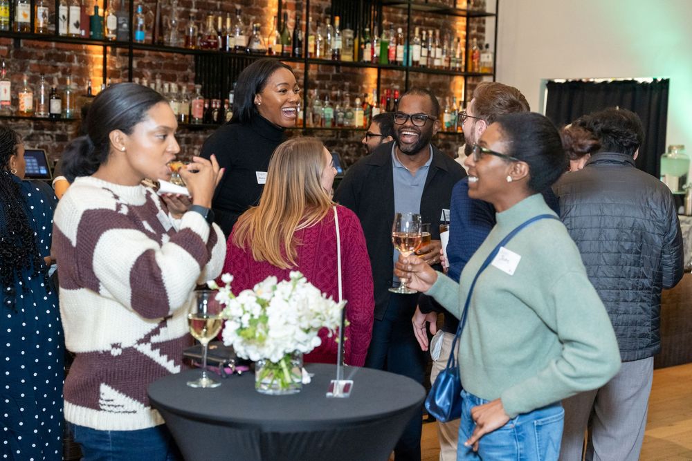 Diverse group of professionals networking at a cocktail reception, holding wine glasses near a floral centerpiece.