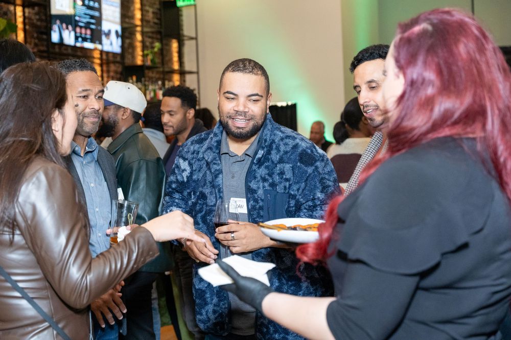 Diverse group of professionals networking and sharing food at an indoor corporate social event.