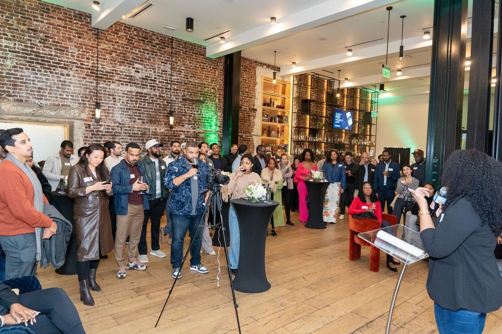 Diverse group of professionals networking at an indoor event in a modern venue with exposed brick walls.