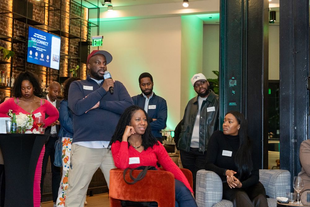 Group of Black professionals gathered at an indoor networking event, some seated and standing.