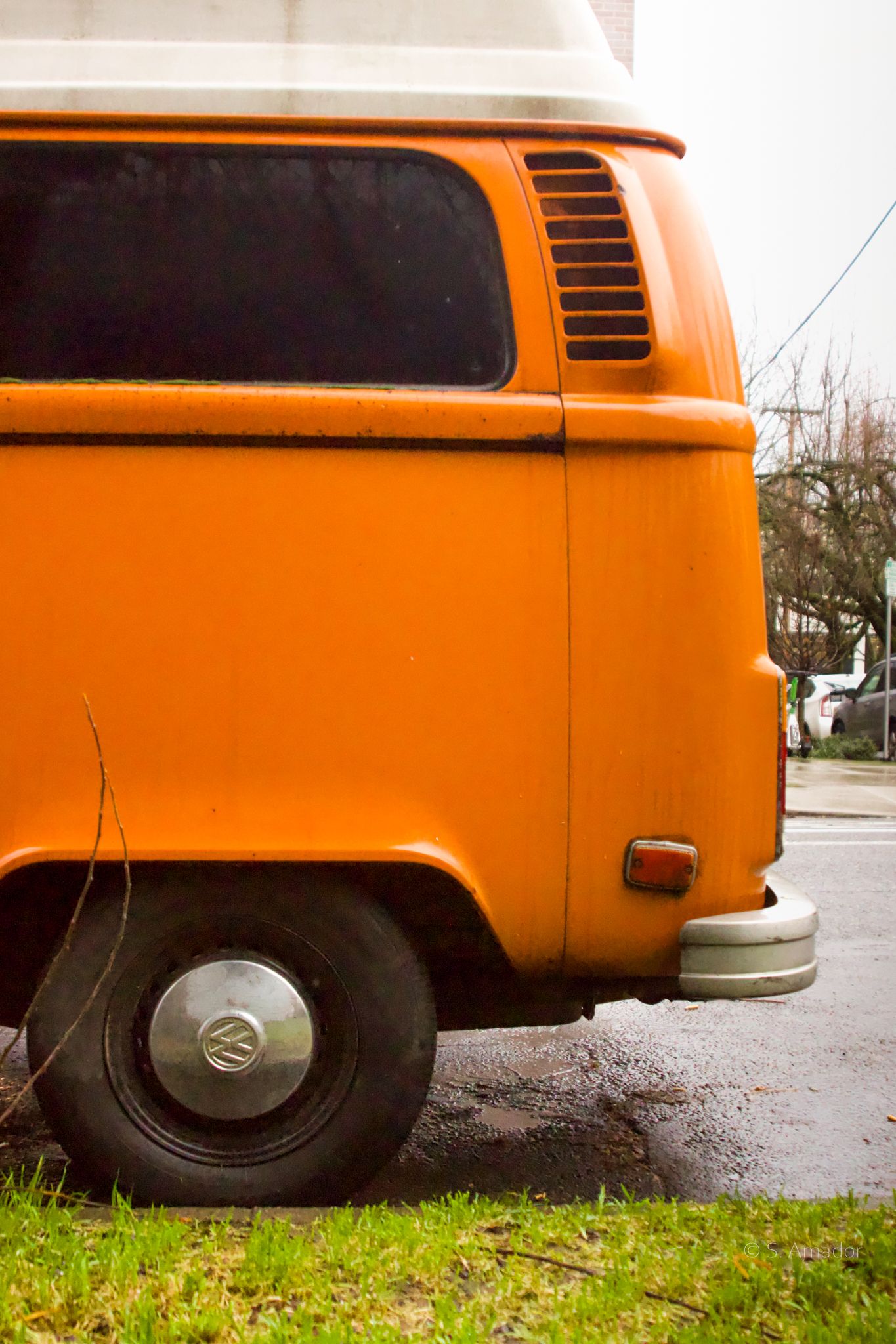 Vintage orange Volkswagen VW Bus van parked on wet street, retro classic vehicle side view.