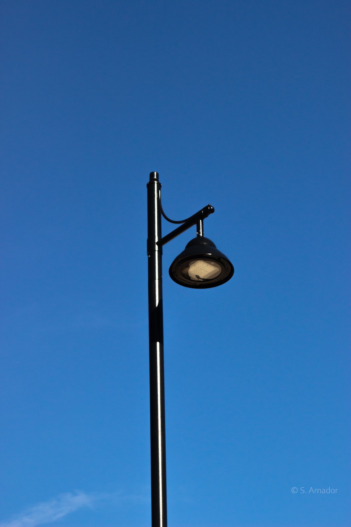 A black street lamp post against a clear blue sky on a sunny day.