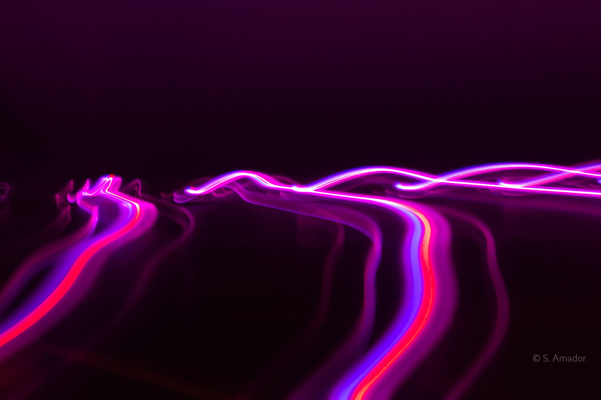 Abstract long exposure pink purple red light trails streaking through dark night background.