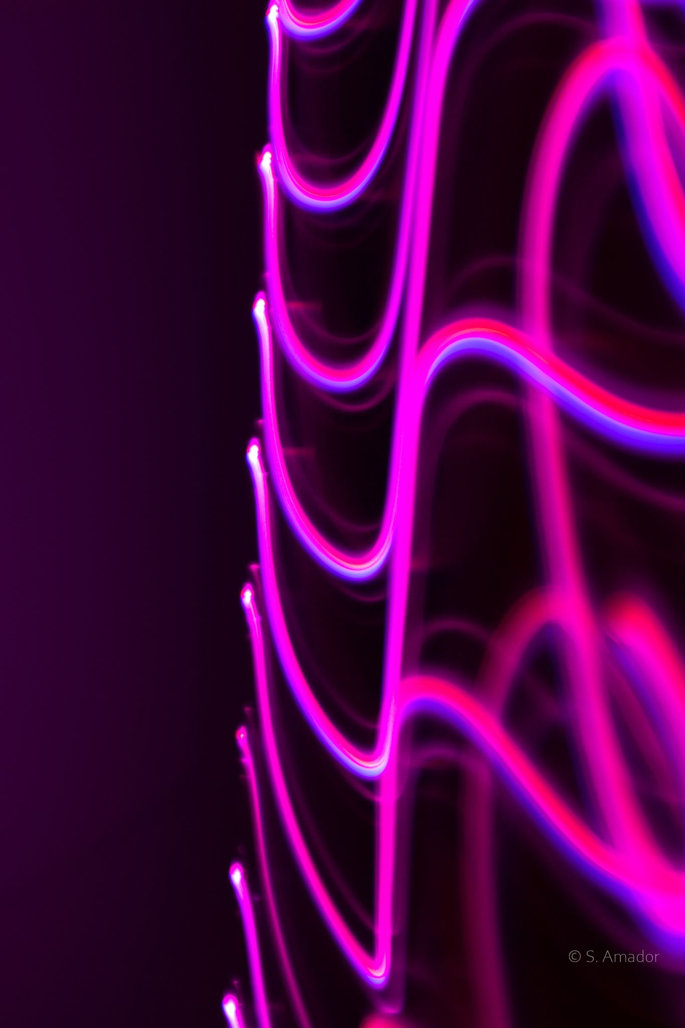 Abstract pink magenta neon light painting waves pattern on dark purple black background.