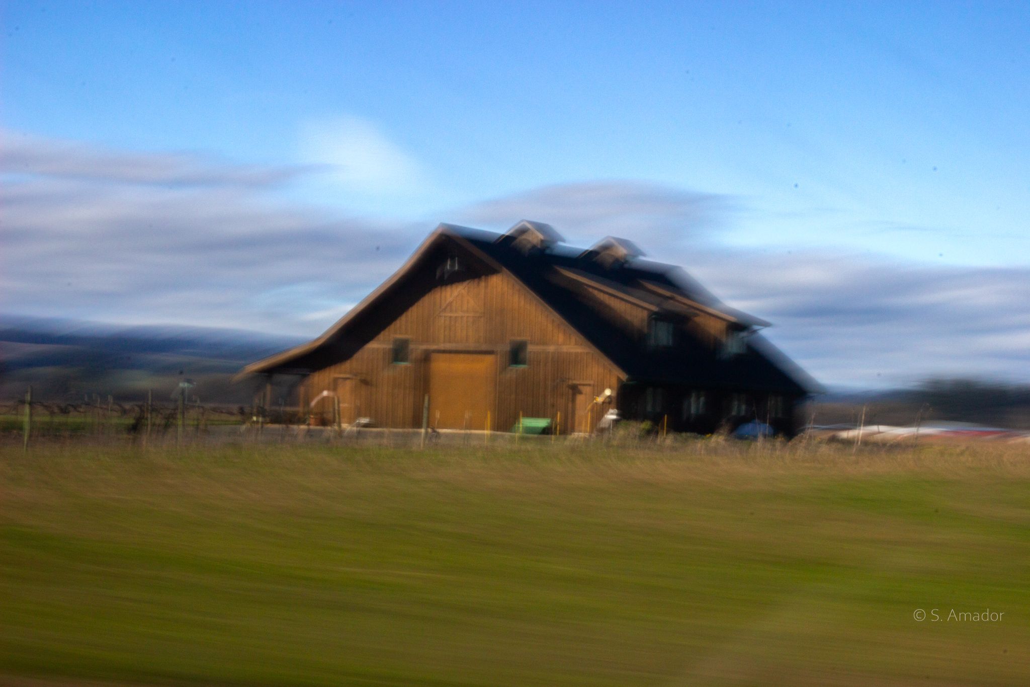 Motion-blurred rustic brown barn under blue sky in rural countryside landscape.
